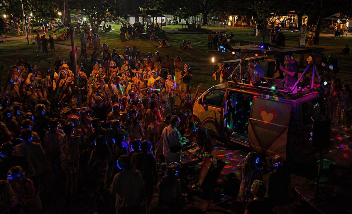 Crowd in glowing headphones dancing beside the DJ van at night
