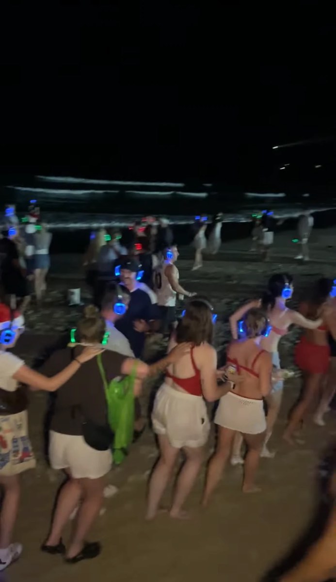 Dancers in headphones on the sand by the water at night